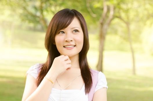 Young Asian college girl student standing on campus lawn, thinking and looking away.