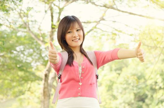 Young Asian college student on campus,  showing thumbs up.