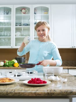 portrait of nice young woman cooking pancakes in kitchen environment