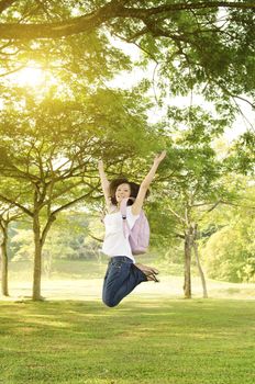 Young Asian college girl student standing on campus lawn, open arms jumping and smiling.