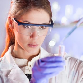 Life scientists researching in laboratory. Focused female life science professional pipetting solution into the glass cuvette. Lens focus on researcher's eyes. Healthcare and biotechnology concept.