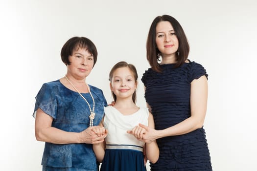 the grandmother, mother and the granddaughter stand in dresses on a white background