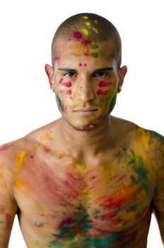 Head and shoulders shot of attractive young man shirtless, skin painted all over with bright Holi colors, looking at camera, isolated on white background