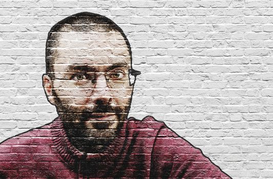 Grinning bearded man in glasses and red sweater with close shave painted on white brick wall