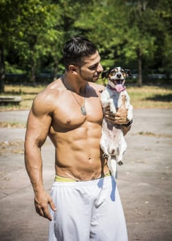 Half Body Shot of a Shirtless Athletic Young Man Carrying One Dog in his Arms and Looking at It