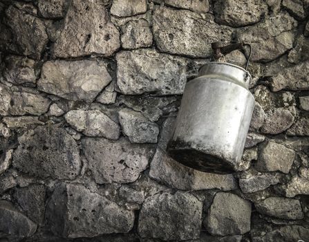 An old fashioned milk tin hanging from an ancient stone wall