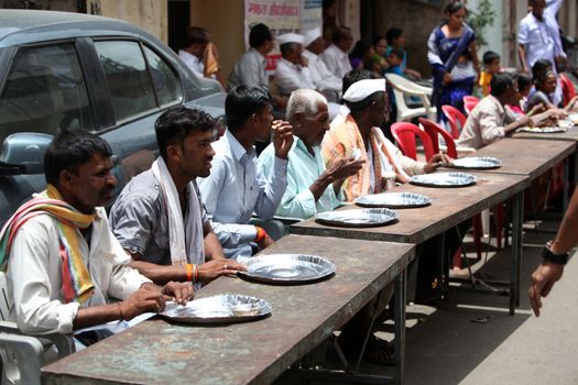 Pune, India - July 11, 2015: Indian pilgrims sitting on table on a sunny day, waiting for food to be served.