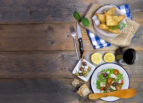 Feta cheese and spinach filo pastries and greek salad laid out on a wooden table