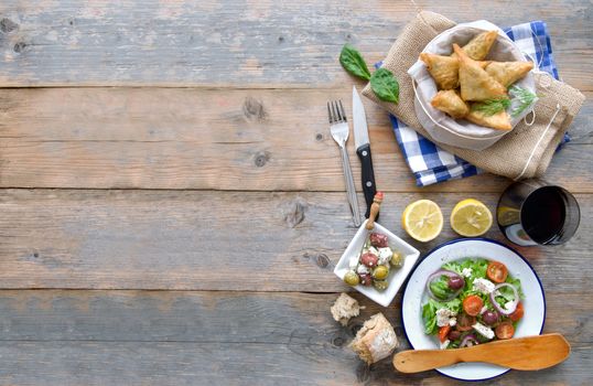 Feta cheese and spinach filo pastries and greek salad laid out on a wooden table