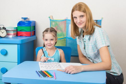 Young girl sitting at a table with a five-year girl and deals with spelling