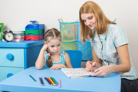 A five-year girl is engaged with adult young beautiful girl sitting at the children table at home