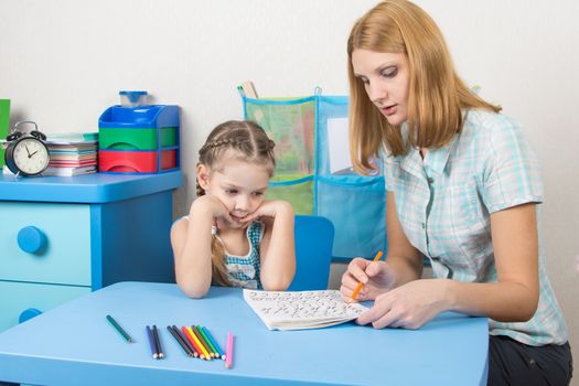 A five-year girl is engaged with adult young beautiful girl sitting at the children table at home