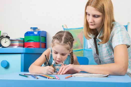 A five-year girl is engaged with adult young beautiful girl sitting at the children table at home