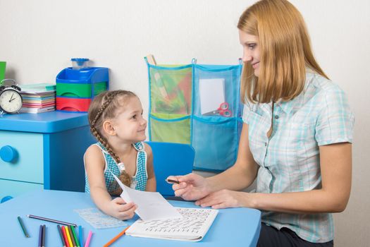 A five-year girl is engaged with adult young beautiful girl sitting at the children table at home