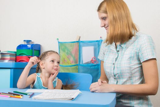 A five-year girl is engaged with adult young beautiful girl sitting at the children table at home