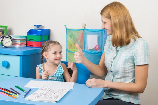 A five-year girl is engaged with adult young beautiful girl sitting at the children table at home