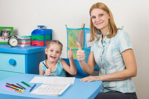 A five-year girl is engaged with adult young beautiful girl sitting at the children table at home