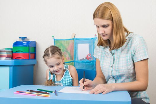 A five-year girl is engaged with adult young beautiful girl sitting at the children table at home