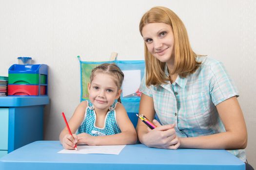 A five-year girl is engaged with adult young beautiful girl sitting at the children table at home