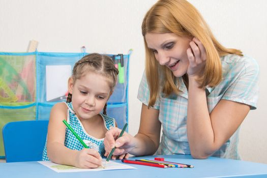 A five-year girl is engaged with adult young beautiful girl sitting at the children table at home