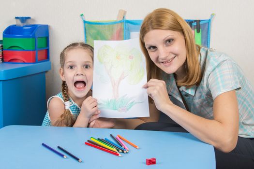 A five-year girl is engaged with adult young beautiful girl sitting at the children table at home