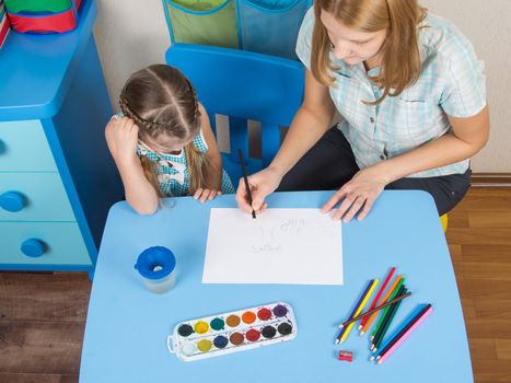 A five-year girl is engaged in drawing with adult young beautiful girl sitting at the children table at home