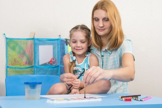 A five-year girl is engaged in drawing with adult young beautiful girl sitting at the children table at home