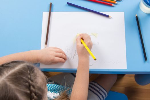 Five-year girl draws pencils sitting at the table at home