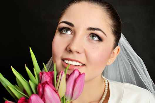 Beautiful, young bride with white veil and flowers bouquet. Female model in studio with black background.