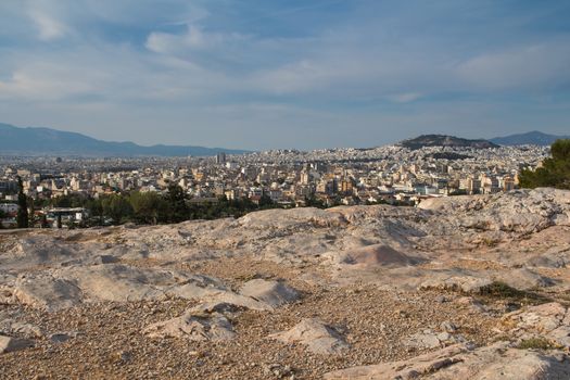 View from a park on a hill on greek capital Athens. Houses climbing up to the hill. Mountains in the background. Cloudy early evening sky.