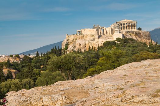 View from a park on the important greek monument: Acropolis, built on the other hill. Line of the soil with stones.  Cloudy early evening sky.