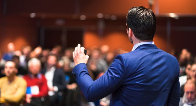 Speaker giving a talk on corporate Business Conference. Audience at the conference hall. Business and Entrepreneurship event.