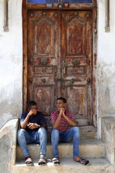 Stone Town, Tanzania - December 30, 2015: Two young people sitting on the steps in the background a traditional wooden door in Stone Town, Zanzibar