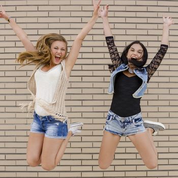 Two beautiful and young jumping in front of a brick wall