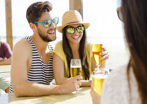 Friends having fun and drinking a cold beer at the beach bar