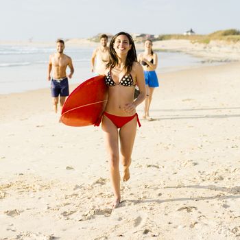 Beautiful and sexy woman running at the beach with her surfboard