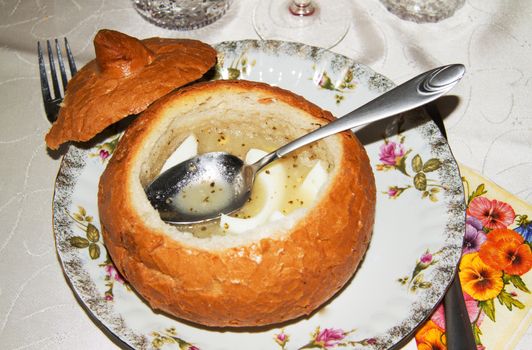 Traditional Polish white borsch in bread with egg and sausage on the table, very popular in Europe, Easter dish. Horizontal view.