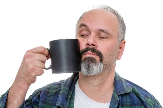 Waking middle aged man dressed in flannel shirt and pajamas and receding hairline with beard tries to drink from a dark coffee mug