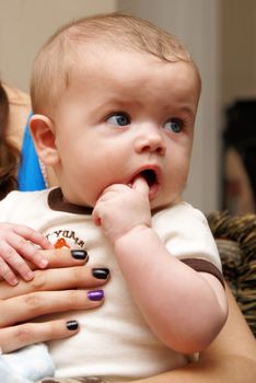 A closeup view of an adorable five month old baby boy sitting upright while on moms lap.