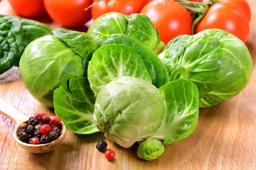 Several heads of fresh wet brussels sprouts, cherry tomatoes, peppers in a small spoon on a wooden table.