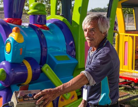 Anderson, California, USA- June 17, 2015: A carnival train employee operates equipment that drives a toy train with children at the Shasta County fair.He operates the ride with the push button control at his fingertips.