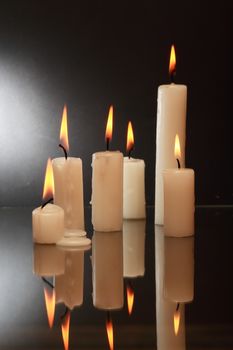 Few lighting candles with reflection on dark background