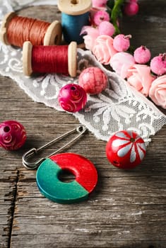 Beads and spool of thread, piece of lace on textured wooden background