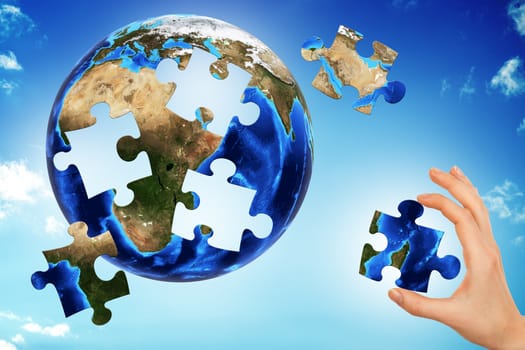 Hand making earth puzzle on blue sky. Elements of this image furnished by NASA