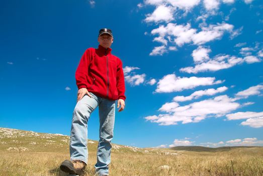 Hiker on the field against sun and cloudscape