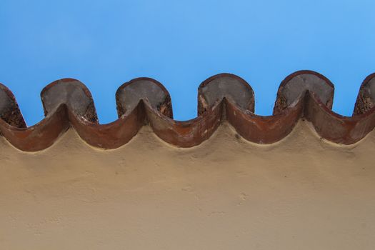 Yellow facade of a house. Edge of a roof creating a pattern. Bright blue sky.