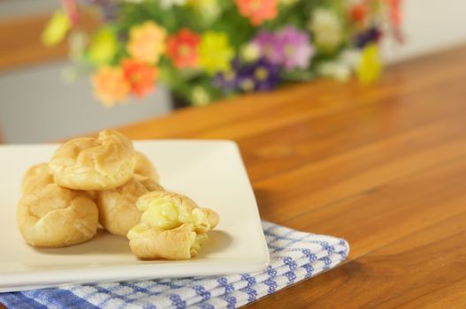 Eclair cream overflow place in plate with blue fabric on wood table and blur flower as background.