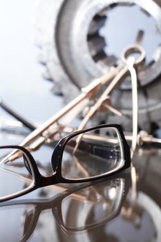 Industrial concept. Spectacles near divider and gear on glass surface against gray background