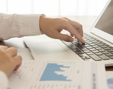 Businessmen are analyzing the data from laptop computer and report.