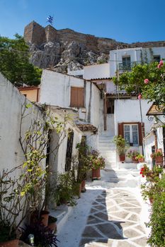 Romantic street of a residential district Plaka, build in the traditional greek style, under the hill with Acropolis. Greek flag in the background. Bright blue sky.